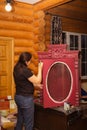 Old Lady in glasses with brush aging wooden cupboard door with red carved ornaments in wooden house. Meticulous process