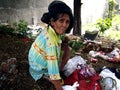 An old lady hunts or scavenges for recyclable materials in a pile of trash in an abandoned lot.