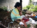 An old lady hunts or scavenges for recyclable materials in a pile of trash in an abandoned lot.