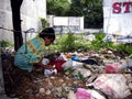 An old lady hunts or scavenges for recyclable materials in a pile of trash in an abandoned lot.