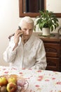 The old lady talking on a cell phone while sitting at a table in the living room.