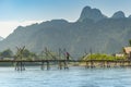 Old lady with umbrella crossing a wooden bridge with beautiful mountain surroundings over the Nam Song River near Vang Vieng, Laos