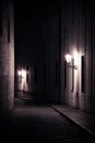 Old lanterns illuminating a dark alleyway medieval street at night in Prague, Czech Republic. Monochromatic photo in vertical. Royalty Free Stock Photo