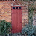 An old, large, red wooden door in a face brick building, most likely a house in a residential district. The entrance way