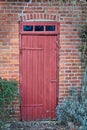 An old, large, red wooden door in a face brick building, most likely a house in a residential district. The entrance way