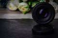 An old lens for a camera with a focal length of 50 mm stands on a table and is turned towards the camera with flowers in the Royalty Free Stock Photo