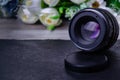 An old lens for a camera with a focal length of 50 mm stands on a table and is turned towards the camera with flowers in the Royalty Free Stock Photo