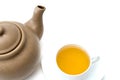Old light brown clay teapot with cracks and scratches on white background. White porcelain cup with green tea is next to it Royalty Free Stock Photo