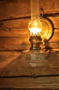 Old lit up oil lamp or lantern hanging on the wall, details of glass and metal. Wall in the background is made of rustic natural Royalty Free Stock Photo