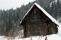 Old log hut at the foot of a hill overgrown with winter forest Royalty Free Stock Photo