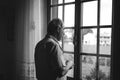 Treviso, Italy - 20 october 2018: old lonely man looking out of window during winter day with serious expression on rainy day Royalty Free Stock Photo