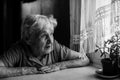 Old lonely woman sitting near the window in his house. Royalty Free Stock Photo