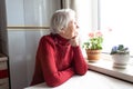 Old lonely woman sitting near the window in his house. Royalty Free Stock Photo