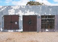Old low run down grey painted storage building with rusty metal bars and closed metal security shutters padlocks on the door