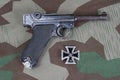 Luger Parabellum handgun and medal Iron Cross on camouflaged background