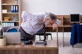 Old male employee suffering from radiculitis at workplace