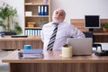 Old male employee suffering from radiculitis at workplace