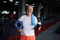 Old man with bottle of water, towel and mat in gym Royalty Free Stock Photo