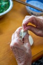 An old man in a Chinese family makes dumplings by hand