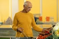 Old man choosing tomatoes from vegetable baskets in supermarket while buying eco groceries