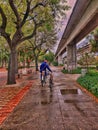 Old man dragging a cycle on his way in a rainy day near the Metro and green trees