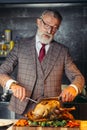 Old-aged handsome man in formal expensive suit cutting out roasted chicken Royalty Free Stock Photo