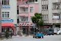 An old man driving his small tractor through a square of the city in daytime