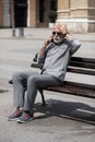 Old man forget something, speak on smartphone and hold hand on head, seating on bench,  stock photo Royalty Free Stock Photo