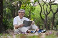 old man with grey hair wears eye glasses sitting under a tree and reading a book in forest park Royalty Free Stock Photo