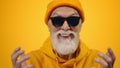 Old man having fun indoor. Joyful guy gesticulating on yellow studio background. Royalty Free Stock Photo