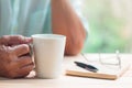 Old man hold white cup of tea or coffee with right hand on light brown wooden table surface Royalty Free Stock Photo