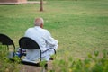 old man isolated sitting alone at iron chair at park from back at evening