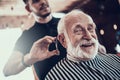 Old man looks at camera while master cuts his hair