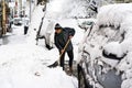Old man, male in winter coat cleaning, shoveling driveway, street from covered falling snow with shovel, residential houses, cars
