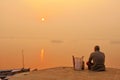 Old man meditates at Varanasi Ganges river bank at sunrise with view of wooden boats and ancient architecture Royalty Free Stock Photo