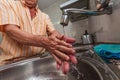 Old man with an orange striped shirt washing his hands in the sink