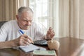 old man with a pencil counts pennies from the pension fund sitting at a table in the room. worried elderly man puts Royalty Free Stock Photo