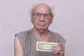 Old man, pensioner who is not combed in gray sleeveless jacket, holds dollar bill in his hand