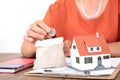 The old man is putting a coin in his pocket and there is a small house model and a calculator on the table