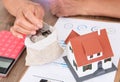 The old man is putting a coin in his pocket and there is a small house model and a calculator on the table