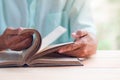 Old man reading book on light brown wooden table surface, flipping movement Royalty Free Stock Photo