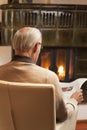 Old man reading newspaper while sitting by a fireplace in a living room Royalty Free Stock Photo
