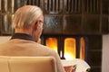 Old man reading newspaper while sitting by a fireplace in a living room Royalty Free Stock Photo