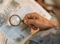Old man reading newspapers with loupe, old repaired fixed magnifying glass