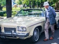 The old man sadly looks at the old yellow american car 1973 Oldsmobile Delta 88 Royale