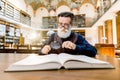 Old man scientist, library worker, reading a book in a library, looking through the magnifying glass. Vintage library