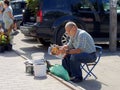 An old man sitting on a folding stool reads a magazine on a street food market