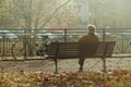 Old man sitting on a wooden bench with a bike near it in a park full of autumn leaves Royalty Free Stock Photo