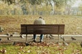 Old man sitting on a wooden bench with doves near it in a park full of autumn leaves Royalty Free Stock Photo