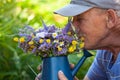 Old man smelling wild flowers in a blue